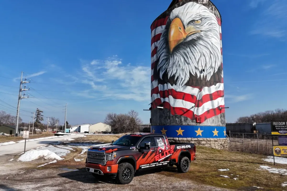 Elite Midnight Roofing branded work truck parked beside a painted eagle silo