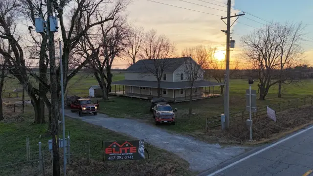 Elite Midnight Roofing yard sign beside a Southwest Missouri farmhouse at sunset