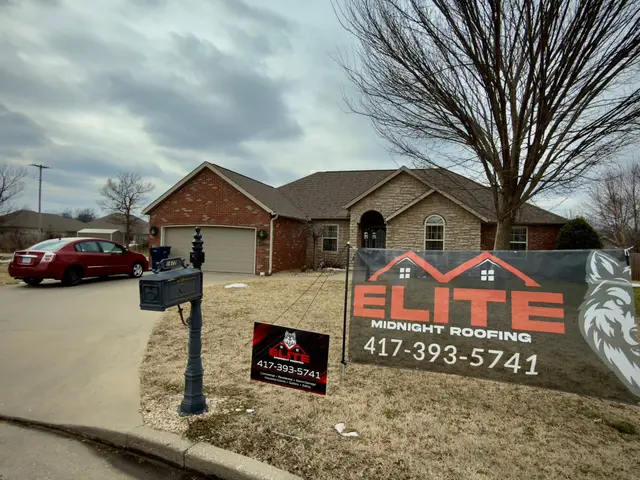 Brick home with an Elite Midnight Roofing banner and yard sign after a roofing project