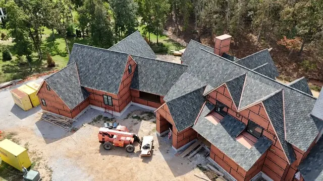 Closer aerial view of the new shingle roof on a large brick home during roofing