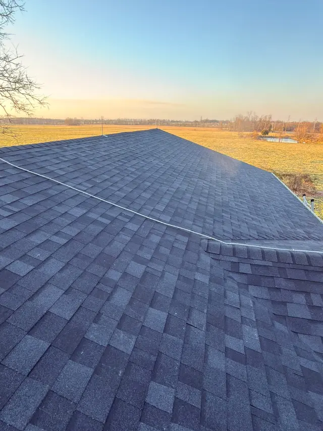 New gray shingle roof at sunset over open farm fields
