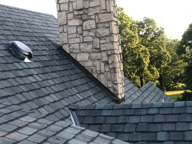 Shingle roof around a stone chimney with a roof vent
