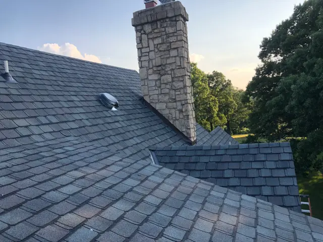 Stone chimney and roof vent on a gray shingle roof
