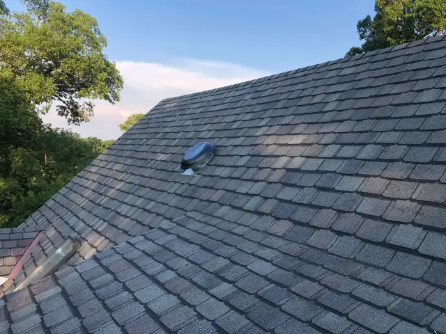 Sloped shingle roof with a pipe vent and trees behind