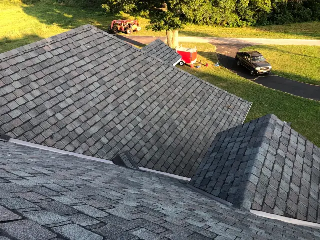 Shingled roof planes and a ridge seen from above, with a driveway below