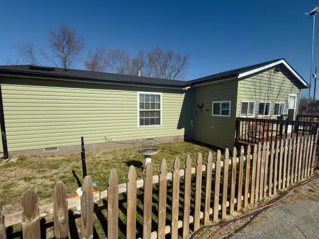 Green vinyl-sided home with a new dark roof and a wooden picket fence
