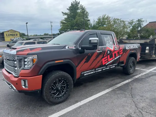 Elite Midnight Roofing branded truck with a dump trailer in a parking lot